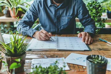 Wall Mural - Person writing on calendar at table with laptop