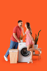 Wall Mural - Happy young couple near washing machine on orange background