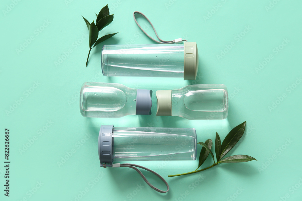 Bottles of water and leaves on green background
