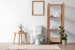 © Pixel-Shot - Interior of restroom with toilet bowl, coffee table and shelving unit near white wall