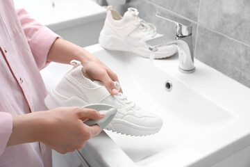 Poster - Woman washing stylish sneakers with brush in sink, closeup