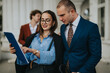 © qunica.com - Confident business professionals discussing project details outdoors. Man and woman in professional attire reviewing documents on clipboard outside office.