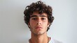 © Khoirul - The face of a young man with curly hair facing the camera against a plain background.