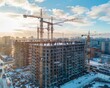 © Preeyanuch - Aerial view of a large construction site with multiple cranes building residential towers in a city during winter with a scenic sky background.