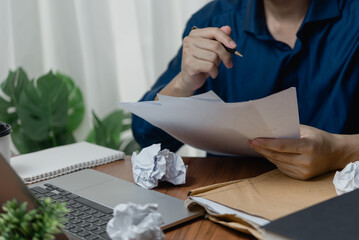 Person reviewing papers at a desk with a laptop and crumpled paper balls