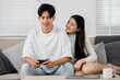 © Satori Studio - A man and woman are sitting on a couch playing a video game. The man is holding a controller and the woman is leaning on him. Scene is relaxed and playful