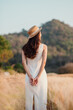 © Satori Studio - A woman wearing a straw hat stands in a field of tall grass. She is looking off into the distance, possibly admiring the scenery or contemplating something. Concept of tranquility and peacefulness