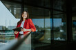 © BGStock72 - Smiling businesswoman in red blazer using tablet at modern office window in daylight