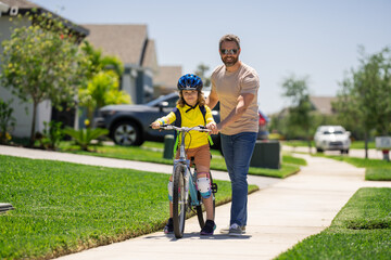 Wall Mural - Father and son in a helmet riding bike. Little cute adorable caucasian boy in safety helmet riding bike with father. Family outdoors summer activities. Fathers day. Childhood and fatherhood.