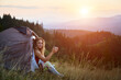 © anatoliy_gleb - Woman traveller camping outdoors at sunset. Beautiful female sitting in tent's entrance on grass with cup of tea. Young tourist hiking, having rest in campsite. Concept of tourism in mountains.
