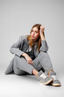 © fotofabrika - Young Woman in a Gray Suit Sitting on the Floor in Studio