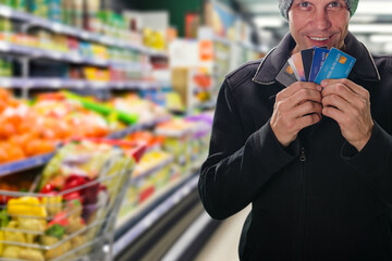 Wall Mural - Happy smiling man shopping at supermarket and showing credit cards as payment method. Easy payment: Hands make supermarket purchases hassle-free with payment cards