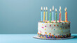 © Mizan Studio - A birthday cake with colorful candles against a pastel blue background.