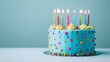 © Mizan Studio - A birthday cake with colorful candles against a pastel blue background.