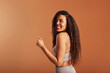 © Flamingo Images - Woman in a bra looking over her shoulder and smiling on an orange background