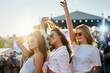 © artiemedvedev - Girls in white tops enjoy summer music festival on sandy beach at sunset. Arms raised, they dance, laugh, celebrate friendship in bright sunlight, crowd, stage in background. Holiday, youth culture.