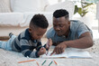© peopleimages.com - Dad, kid and help with homework in home for education, learning and support with care. Black parent, school work and teaching for child development or growth with project, art and creativity on floor