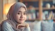 © Leli - A woman in a hijab sitting in front of a bookshelf, deep in thought