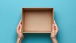 © horizon - A person holding out an empty cardboard box against blue background, top view.