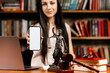 © Vladislav - A female lawyer in her office holds a phone with a white screen in her hands. An isolated place for your advertising. Concept of legal work, business and modern technologies.