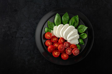 Wall Mural - Mozzarella with basil and cherry tomatoes on a black stone background.