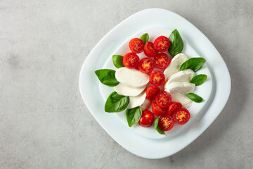 Wall Mural - Mozzarella with basil and cherry tomatoes on a white stone table.