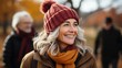 © AS Photo Family - A radiant senior woman smiles warmly wearing a wintry hat and scarf, with a vibrant autumnal background and gently blurred surroundings