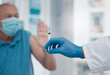 © peopleimages.com - Elderly man, stop and hand with vaccine in clinic for healthcare, wellness and prevention for risk. Doctor, needle and male person with mask for protection, medicine and safety for virus in hospital
