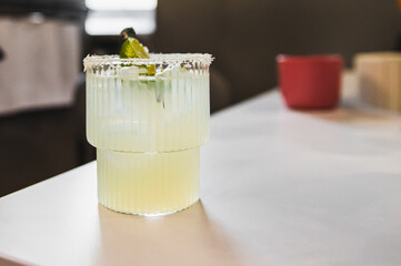 A close-up of a classic margarita cocktail with a salted rim and lime garnish on a bar counter.