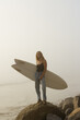 © Nicole Mason/Stocksy - young woman holding surf board at the coast