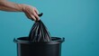 © SKIMP Art - Close up of hand putting a black garbage bag into a trash bin isolated on a blue background, in a closeup view Generative AI