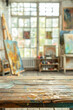 © grey - A wooden table in the foreground with a blurred background of an art studio. The background includes easels with canvases, paintbrushes, palettes, colorful paintings on the walls, and shelves