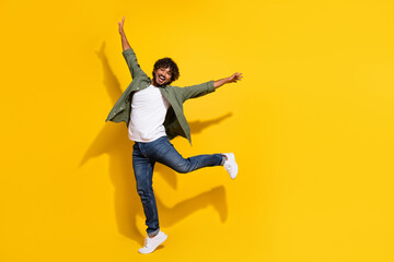 Wall Mural - Portrait photo of young funny mexican guy raised arms overjoyed in trendy khaki shirt and jeans isolated on yellow color background