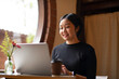 © Wasana - A woman is sitting at a table with a laptop and a cup of coffee