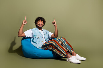 Sticker - Full body photo of attractive young man sit beanbag point up empty space dressed stylish denim clothes isolated on khaki color background