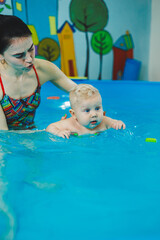 Wall Mural - A little 8-month-old boy is learning to swim in the pool with a coach.