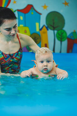 Wall Mural - A little 8-month-old boy is learning to swim in the pool with a coach.