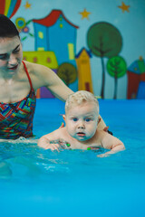 Wall Mural - A little 8-month-old boy is learning to swim in the pool with a coach.