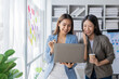 © ArLawKa - Two young Asian businesswomen work on laptop computers in the office with reports. Colleagues discuss financial data in document analysis of new marketing projects.