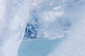 Winter natural background with fragments of blue ice and heaps of pieces of ice floes on Lake Baikal on a sunny frosty day. Abstract cold background, mock up. Harsh lifeless environment