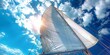 © aicandy - A breathtaking view captures the majestic sail of a boat gliding through a canvas of bright blue sky and fluffy clouds, illuminated by the radiant sun