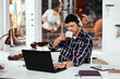 © peopleimages.com - Laptop, coffee and man with headphones in workshop for streaming audio, networking or email. Caffeine, music and employee at desk for manufacturing, forge metal or welding steel in blacksmith factory