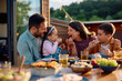 © Drazen - Happy family having fun while eating donuts at picnic table on  patio.