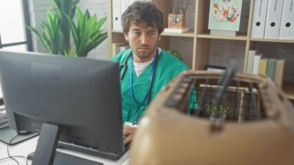 Canvas Print - A focused veterinarian in scrubs works on a computer in a clinic office, with a pet carrier in the foreground.