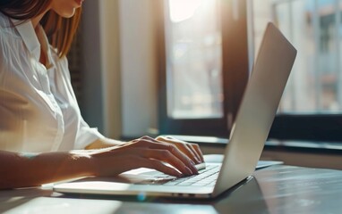 Businesswoman typing on laptop in sunlit office.