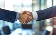 © OLGA - Close-up of a handshake between two businessmen in a blurred office setting.