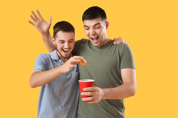 Wall Mural - Male friends with beer and ball on yellow background