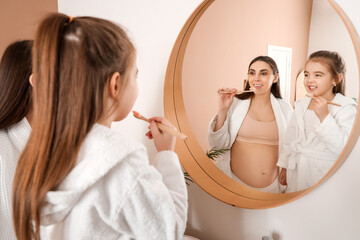 Sticker - Little girl with her pregnant mother brushing teeth near mirror in bathroom