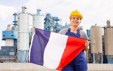 Happy woman waving flag of France against the background of a modern factory