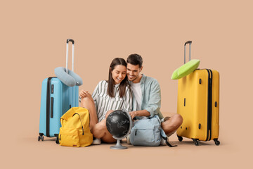 Wall Mural - Beautiful young happy couple of tourists with suitcases, backpacks and globe sitting on brown background